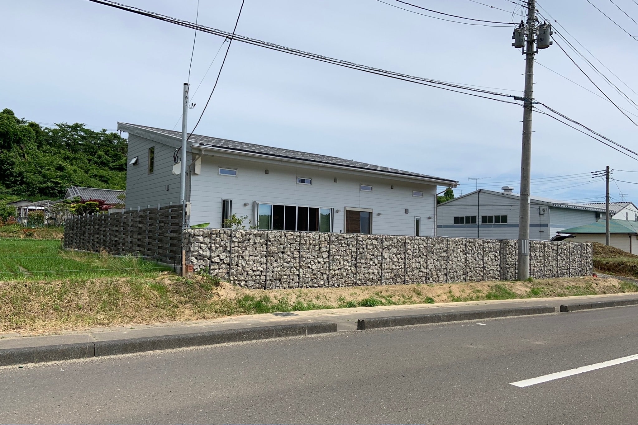 道路から見た建物と、その周囲を長く囲うガビオン
